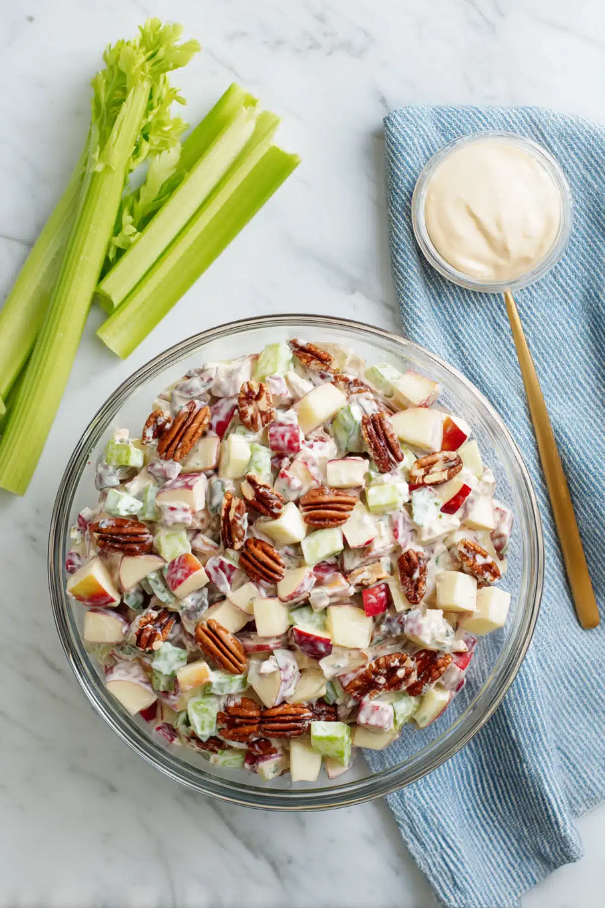 Chicken salad with diced apples, crunchy pecans, and celery in creamy dressing served in a clear glass bowl on marble.

