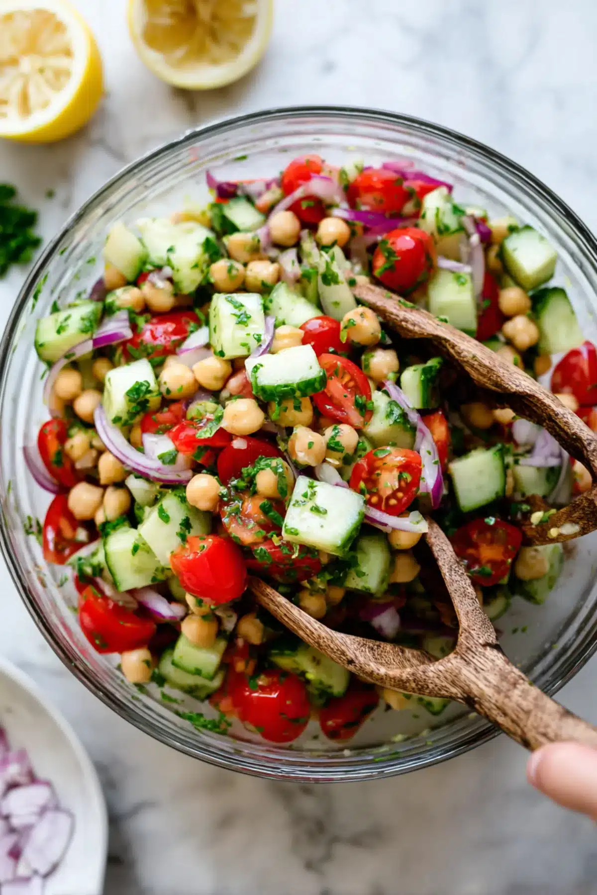 Chickpea cucumber salad with cherry tomatoes, red onion, and parsley in a glass bowl with lemon in the background