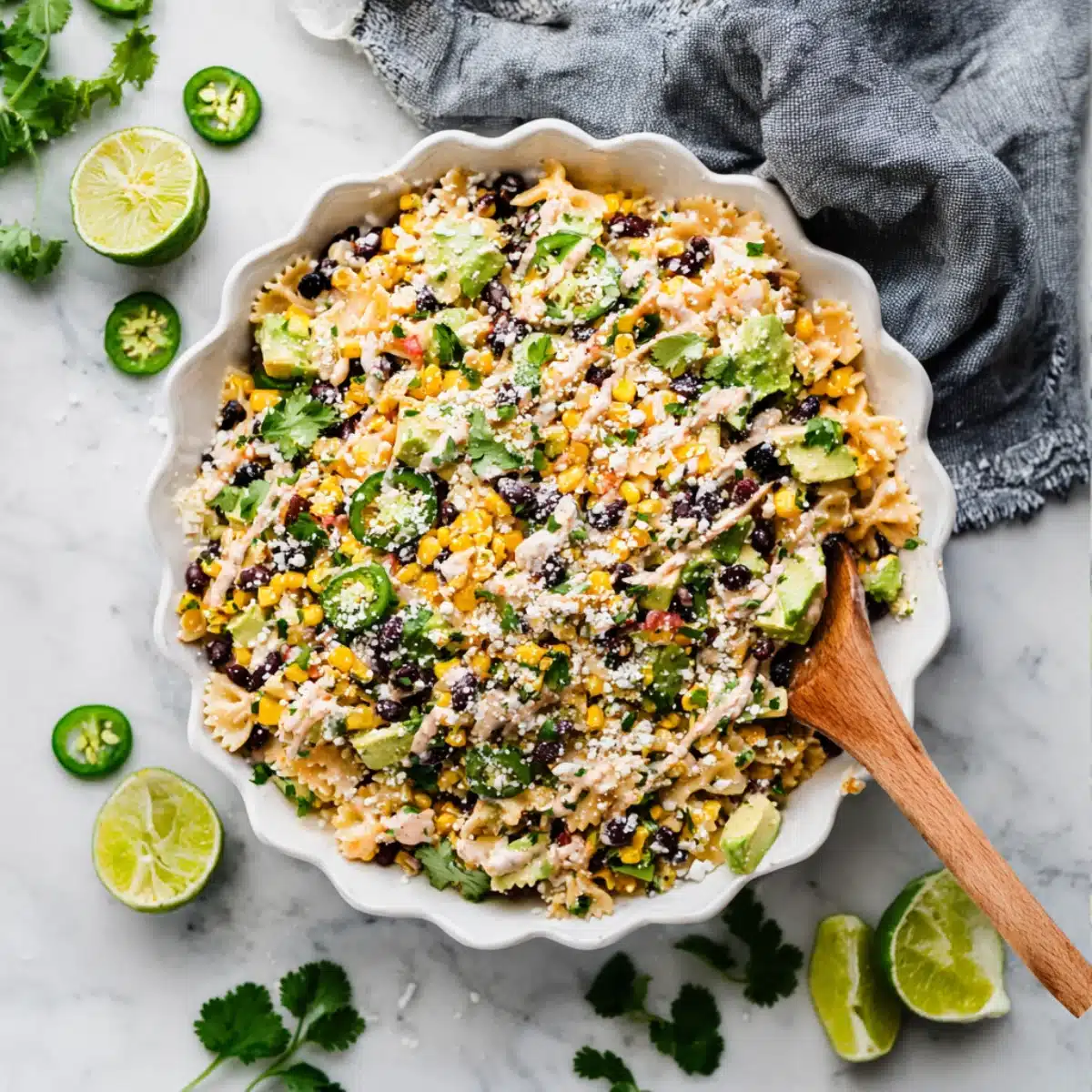 Creamy Mexican Street Corn Pasta Salad with avocado, black beans, corn, jalapeños, and cheese in a scalloped white bowl
