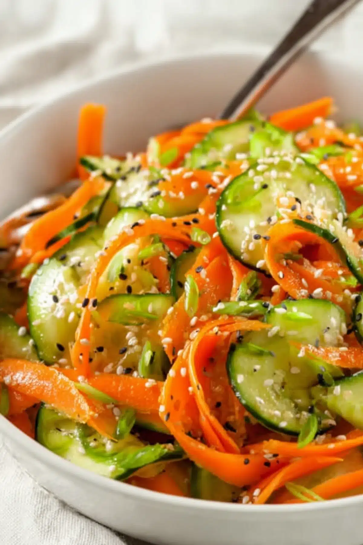 Close-up of cucumber carrot salad with sesame seeds and scallions in a white bowl, showing vibrant colors and textures.