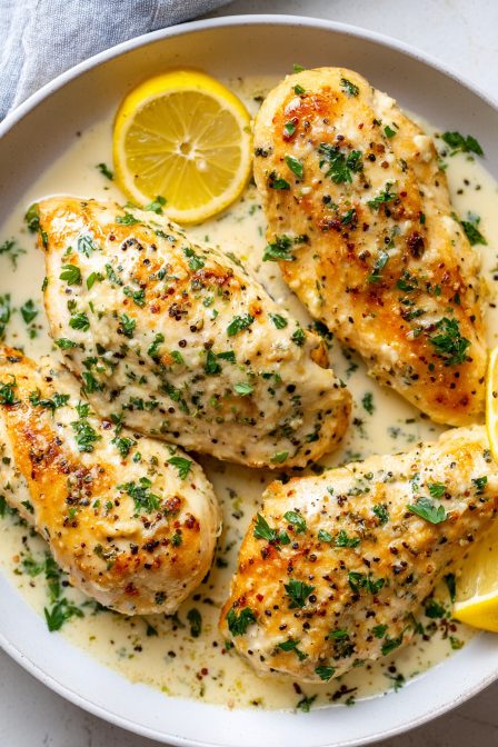 Tender garlic parmesan chicken breasts simmered in creamy parmesan sauce with herbs and lemon slices in a skillet