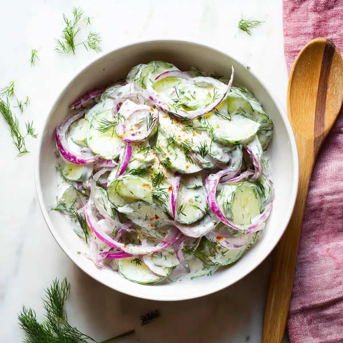 Greek yogurt cucumber salad topped with red onions, dill, and spices served in a white bowl on a marble surface