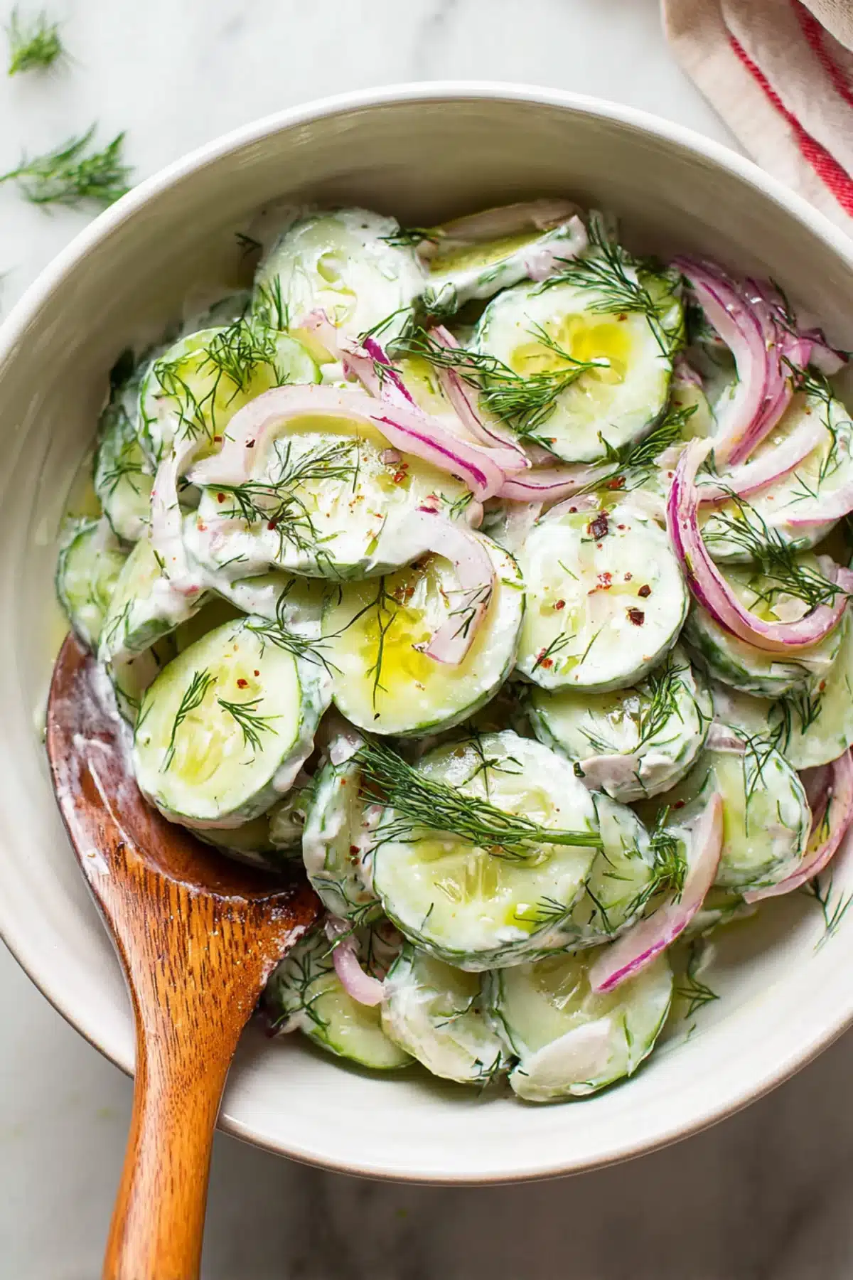 Cucumber slices with creamy Greek yogurt, fresh dill, and red onions served in a white bowl with olive oil drizzle