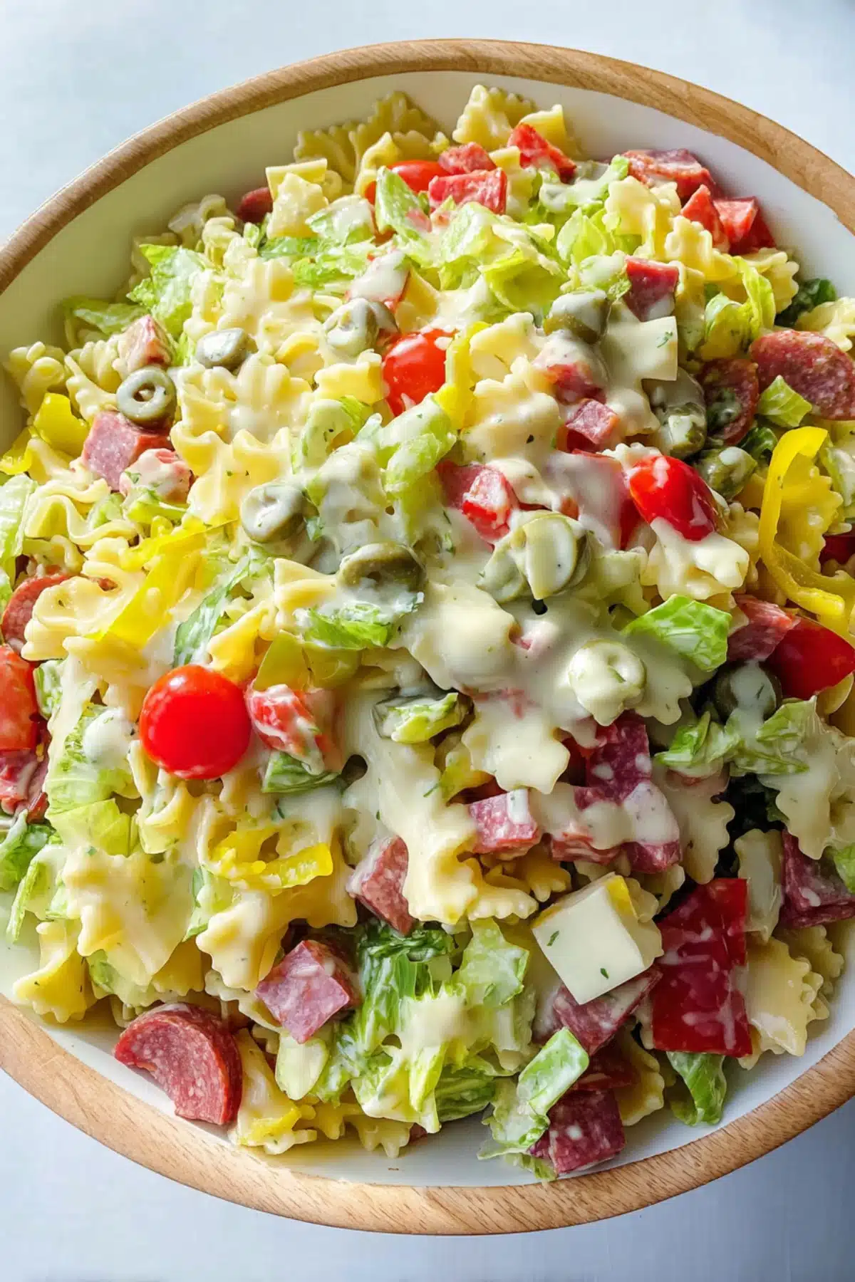 Grinder pasta salad with creamy dressing, bowtie pasta, lettuce, cherry tomatoes, salami, and banana peppers in a bowl