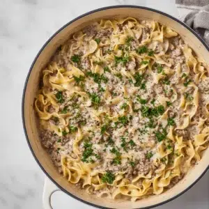 Creamy ground beef stroganoff with egg noodles, topped with parsley, served in a large white skillet.