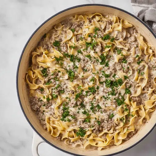 Creamy ground beef stroganoff with egg noodles, topped with parsley, served in a large white skillet.