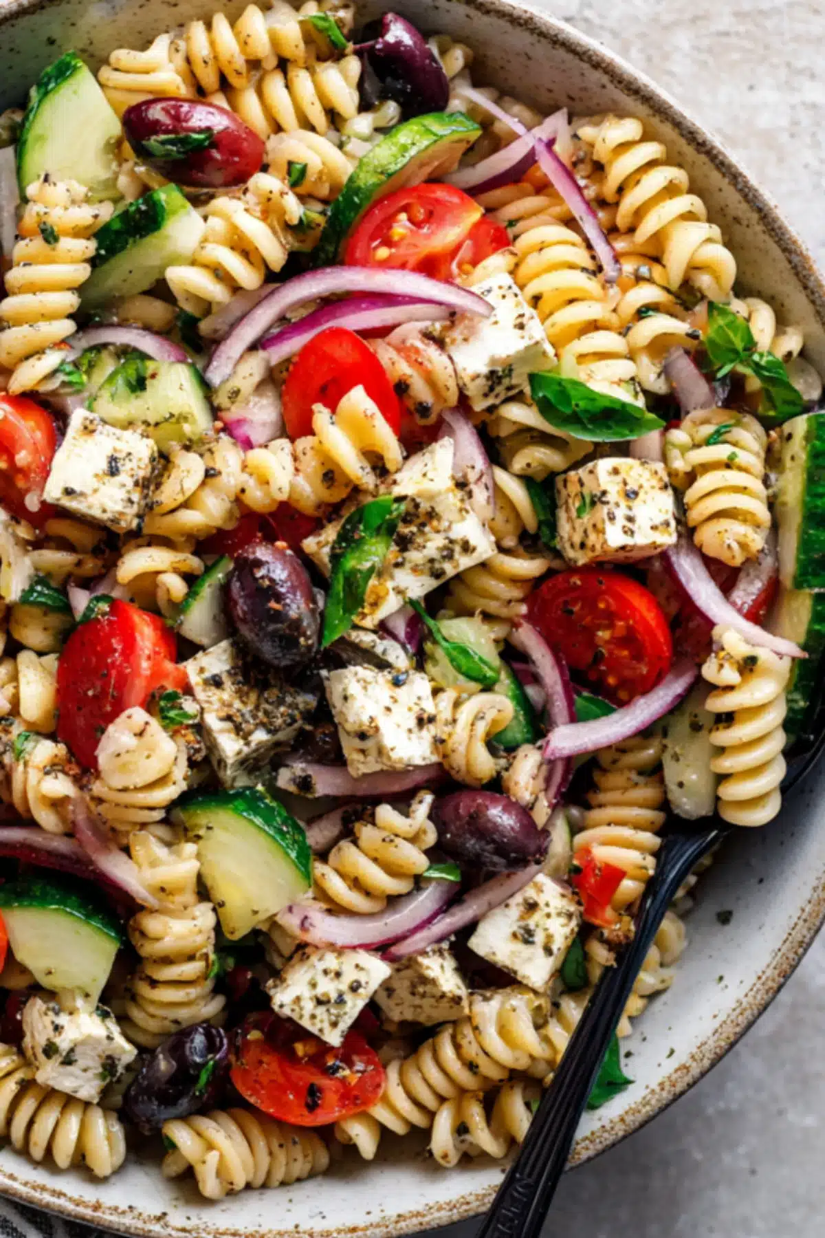 Colorful high protein pasta salad with feta, rotini, cherry tomatoes, olives, cucumbers, and fresh herbs.