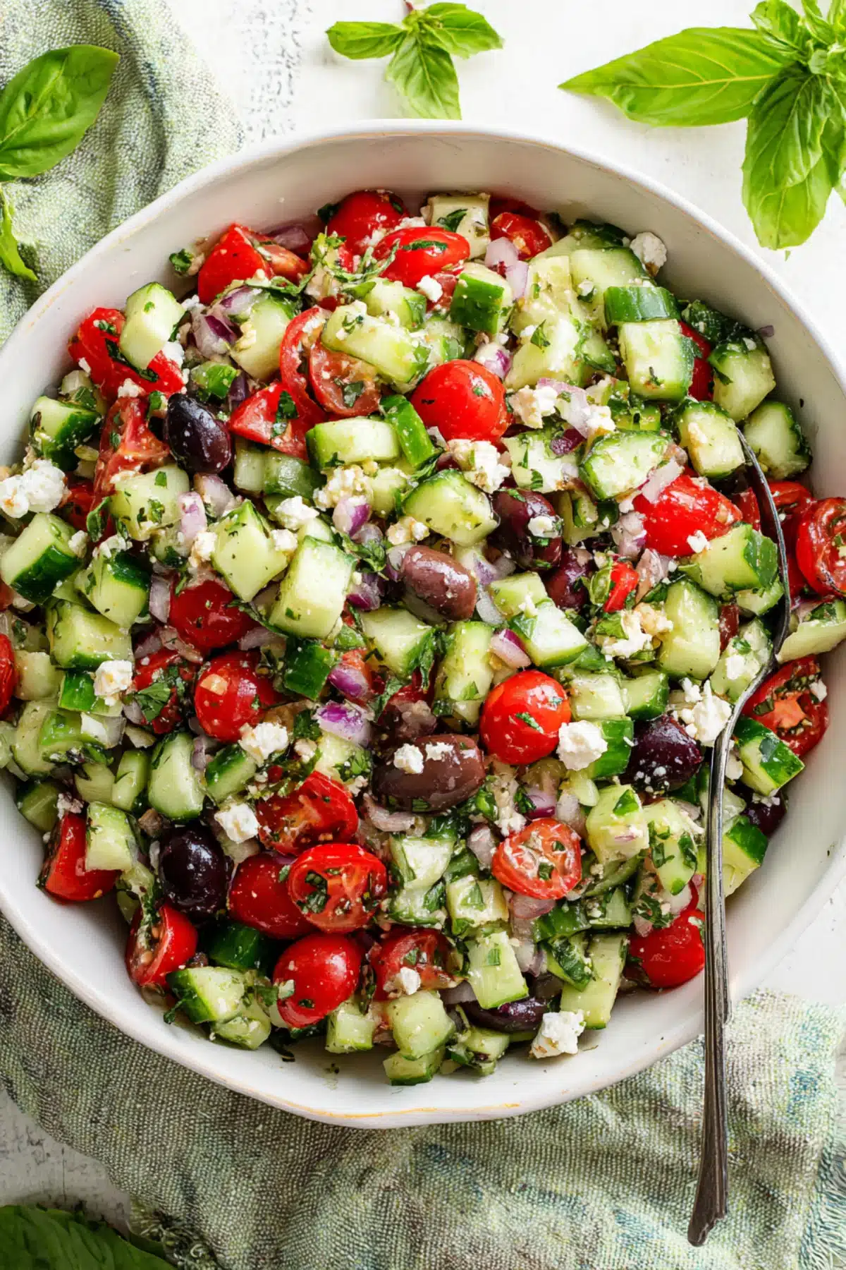 Fresh Mediterranean cucumber salad with cherry tomatoes, feta cheese, red onion, and Kalamata olives in a white bowl.