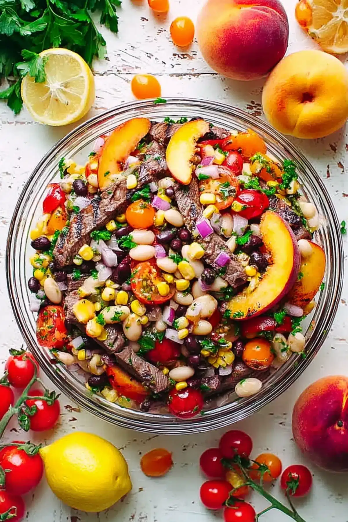 Colorful steak dense bean salad with peaches, corn, cherry tomatoes, red onion, and herbs in a glass bowl