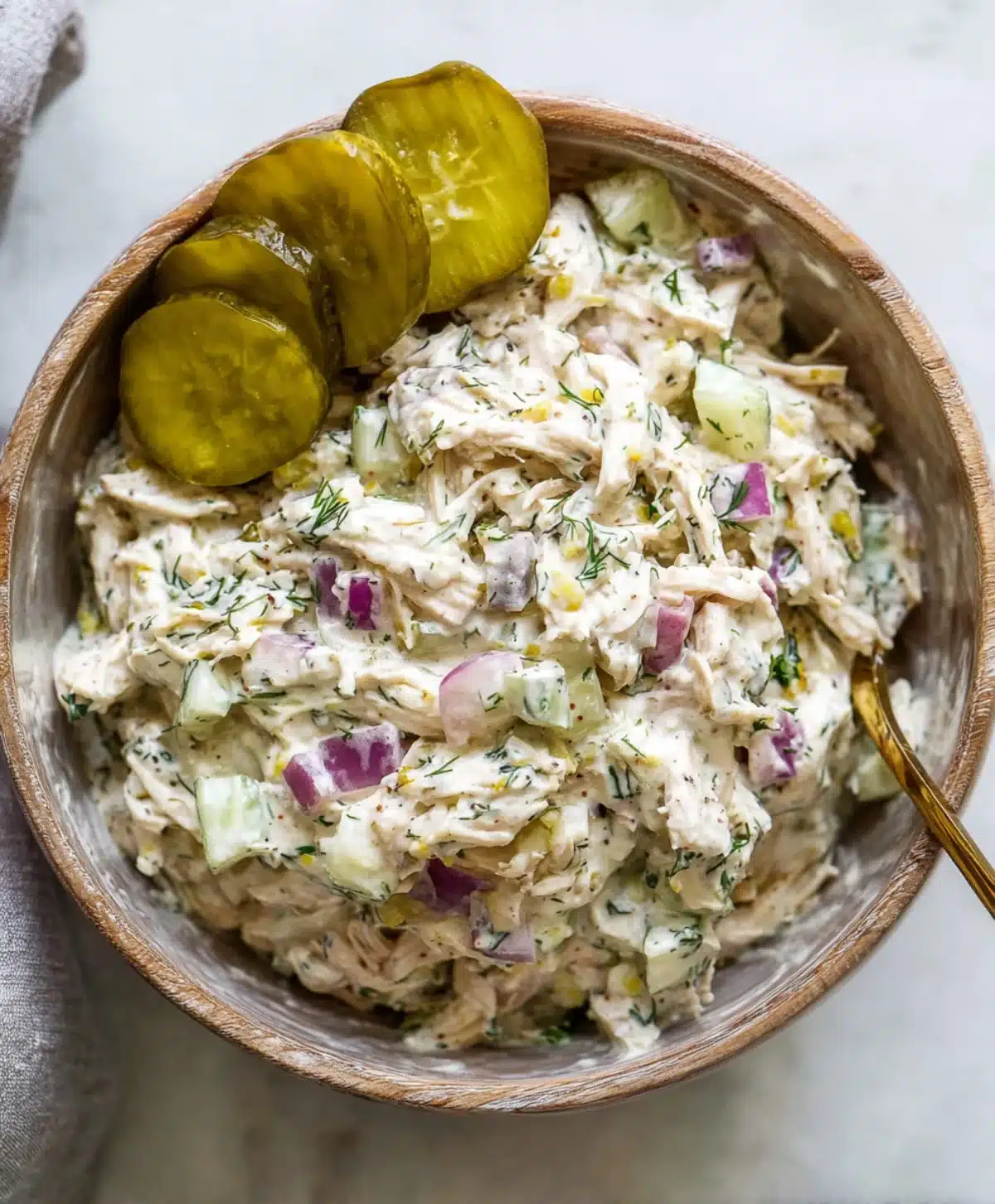 Bowl of creamy dill pickle chicken salad with red onions, cucumbers, and pickle slices, topped with fresh dill