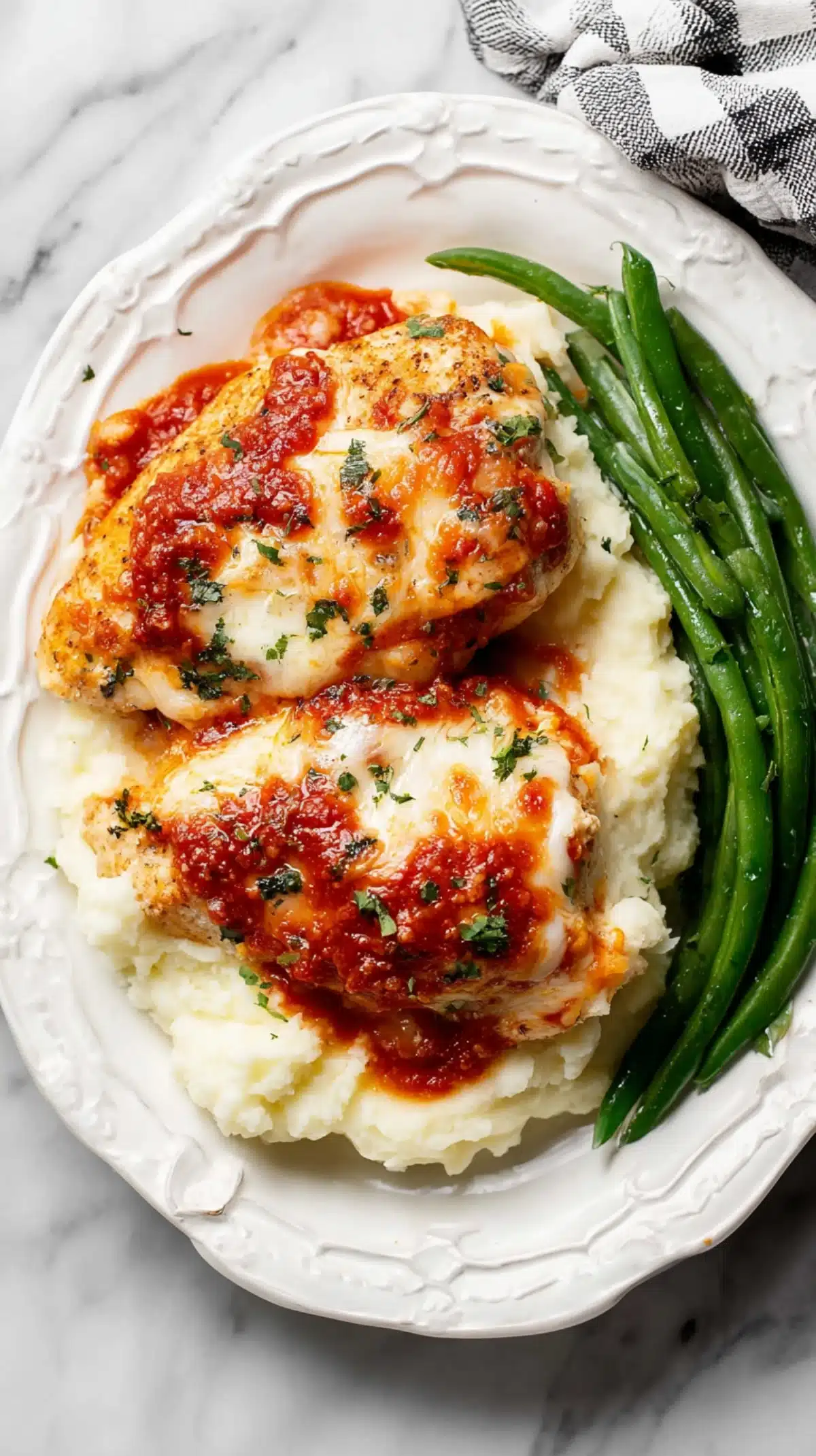 Cheesy chicken bake served over mashed potatoes with green beans on a white plate, garnished with herbs