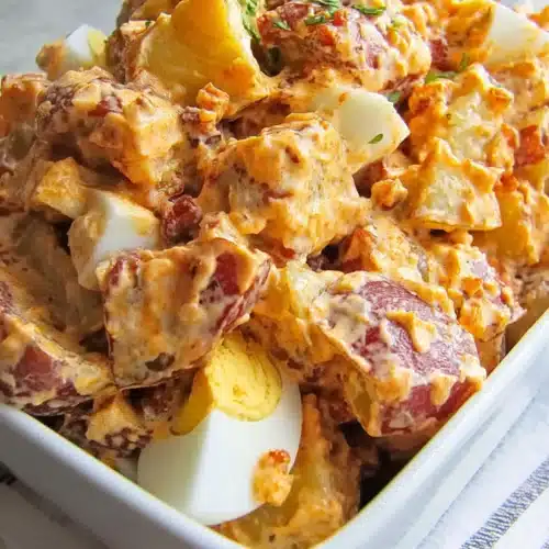 BBQ potato salad with smoky dressing, red potatoes, chopped bacon, and sliced boiled eggs in a white dish