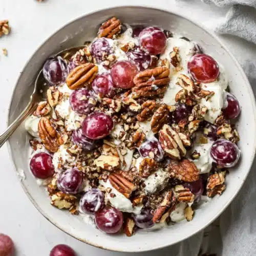 Sweet grape salad with creamy dressing and chopped pecans served in a white bowl on a light countertop