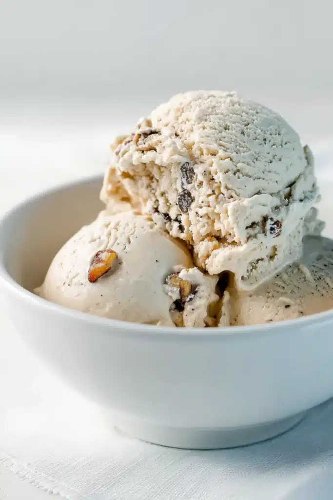 Scoops of classic black walnut ice cream with visible walnut chunks served in a white bowl on a white napkin
