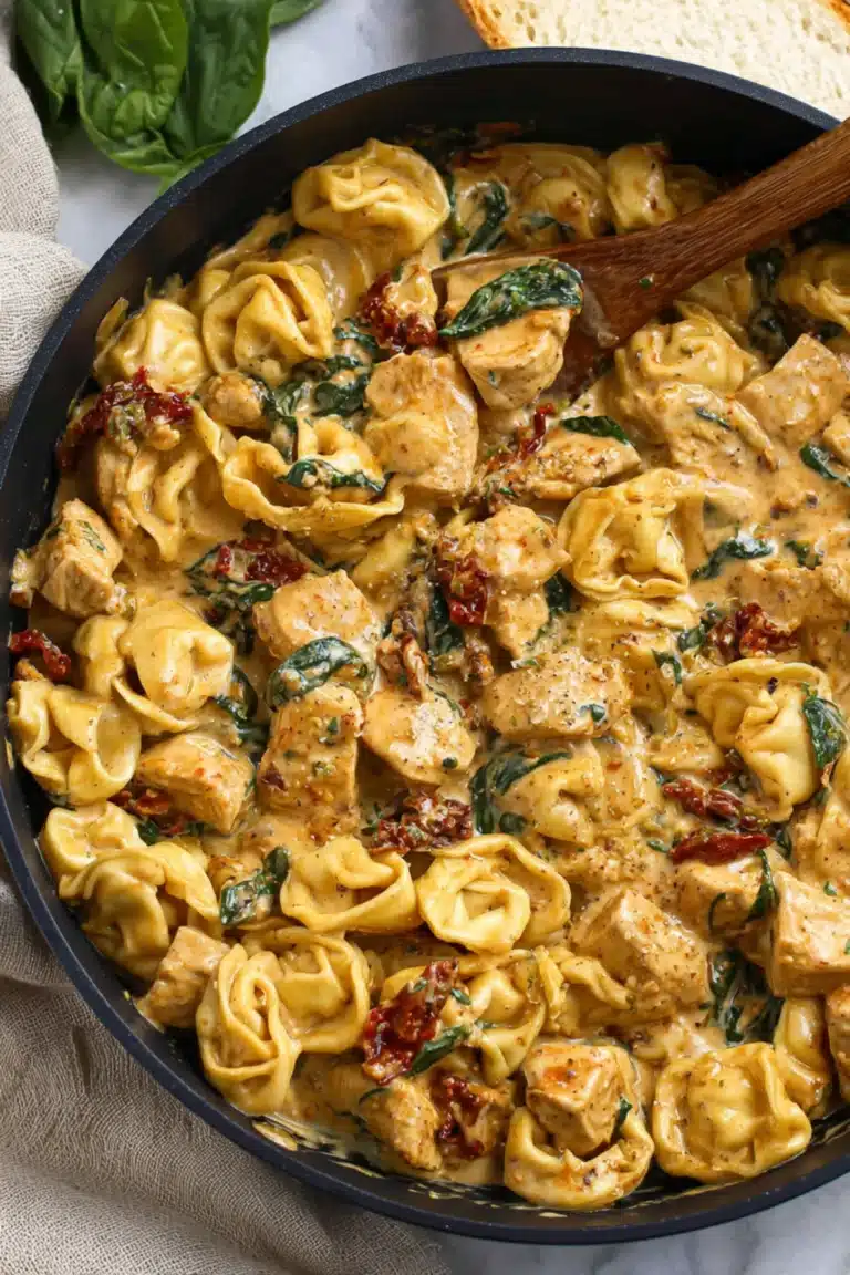 Creamy tortellini pasta with golden chicken cubes, spinach, and sun-dried tomatoes in a rich sauce inside a black skillet