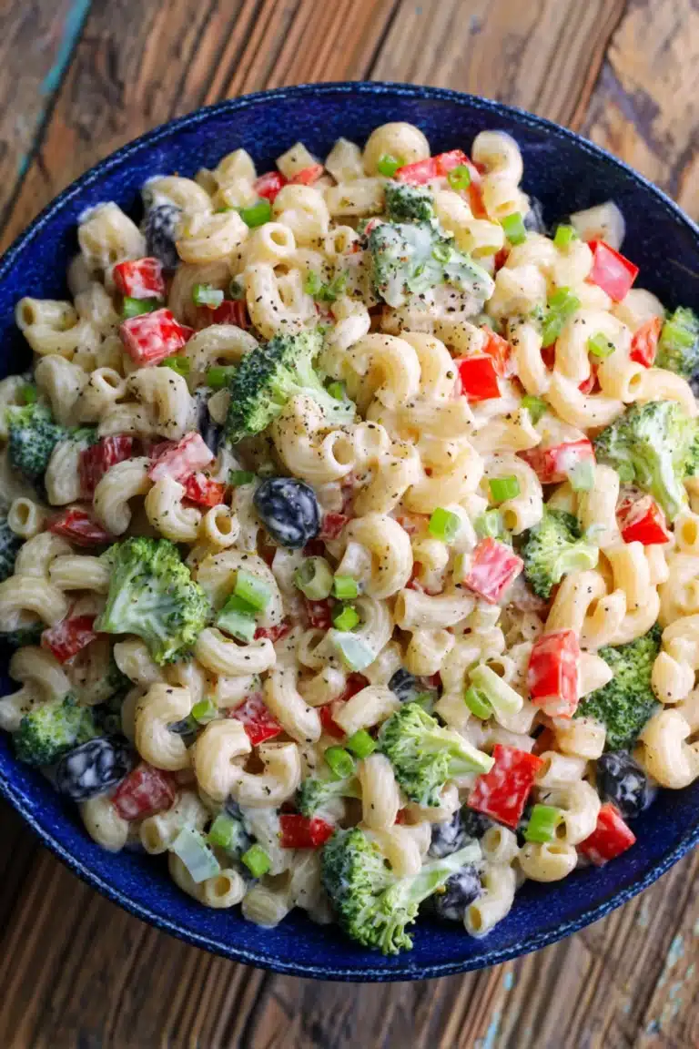 Creamy pasta salad with broccoli, red bell peppers, and black olives in a blue bowl.