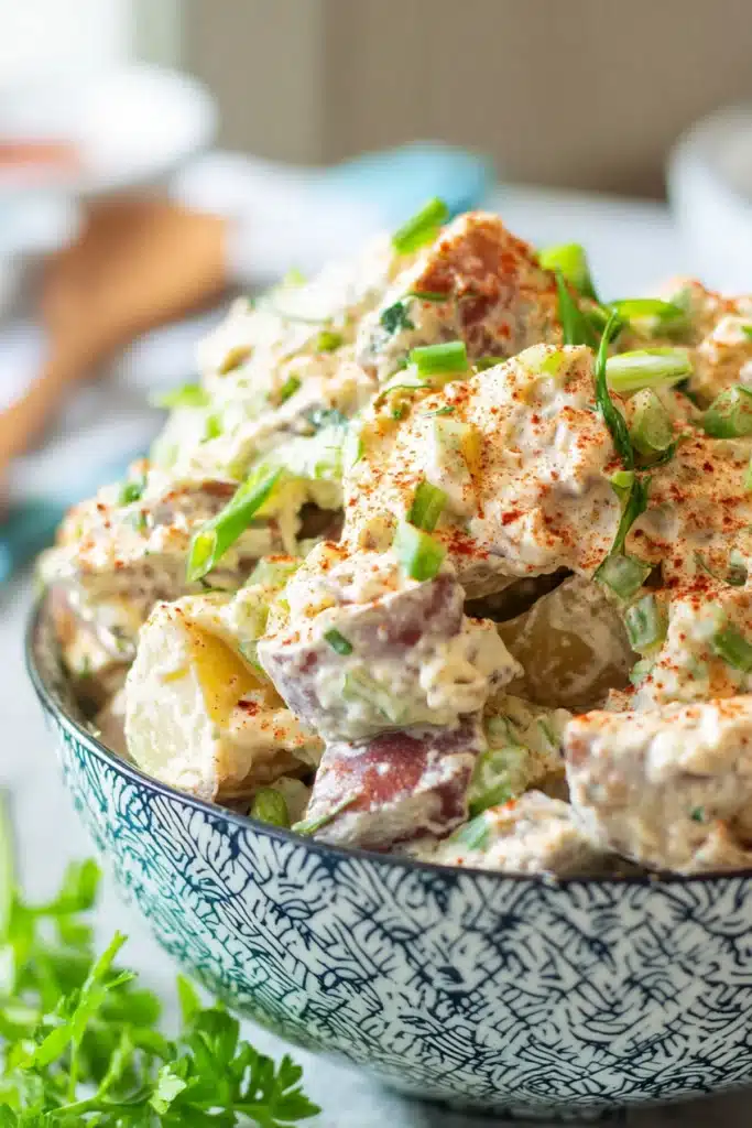 Creole potato salad with creamy dressing, red potatoes, paprika, and green onions in a patterned bowl