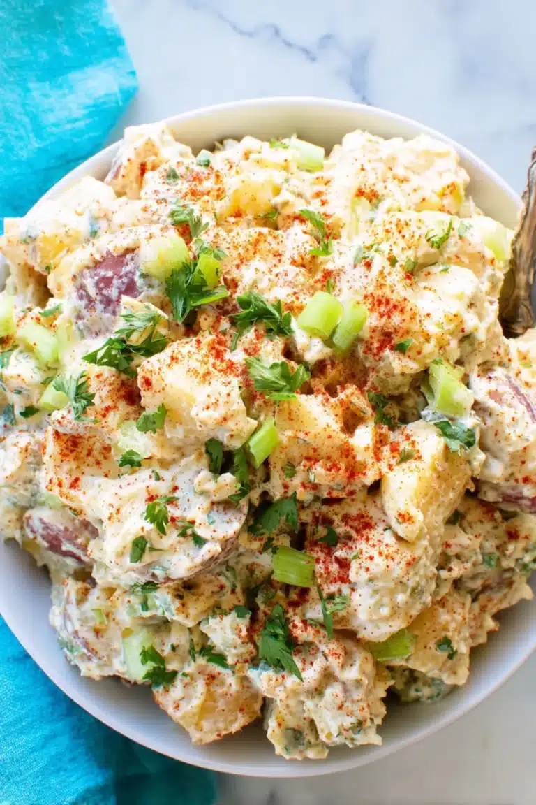 Creamy Creole potato salad with red potatoes, chopped green onions, paprika, and fresh parsley in a white bowl