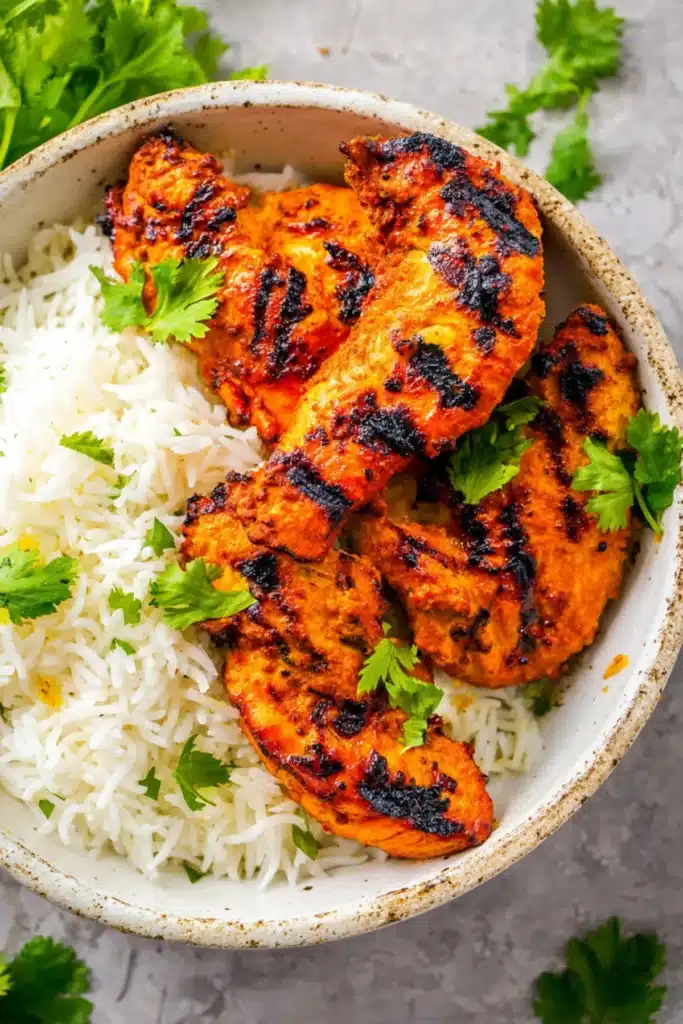 Juicy grilled tandoori chicken with aromatic spices served on fluffy basmati rice, garnished with fresh cilantro leaves