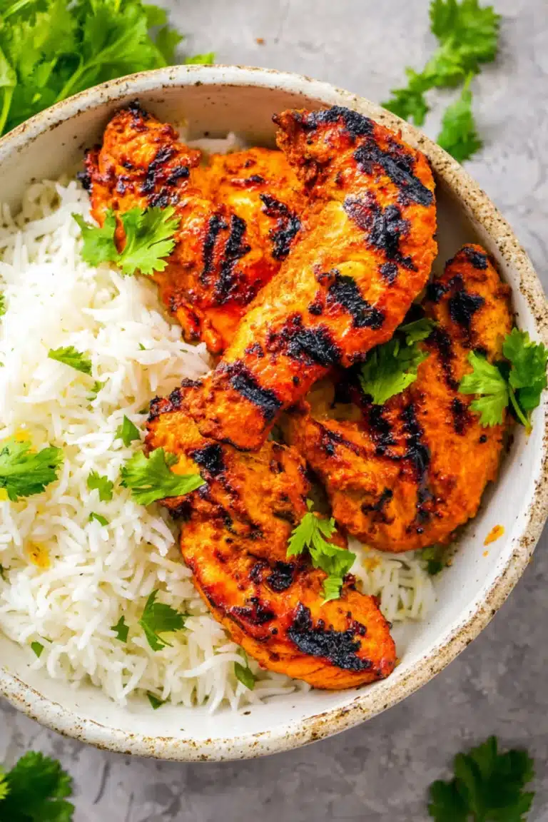 Juicy grilled tandoori chicken with aromatic spices served on fluffy basmati rice, garnished with fresh cilantro leaves