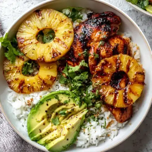 Grilled Hawaiian BBQ chicken with pineapple, avocado slices, and cilantro over steamed white rice in a bowl