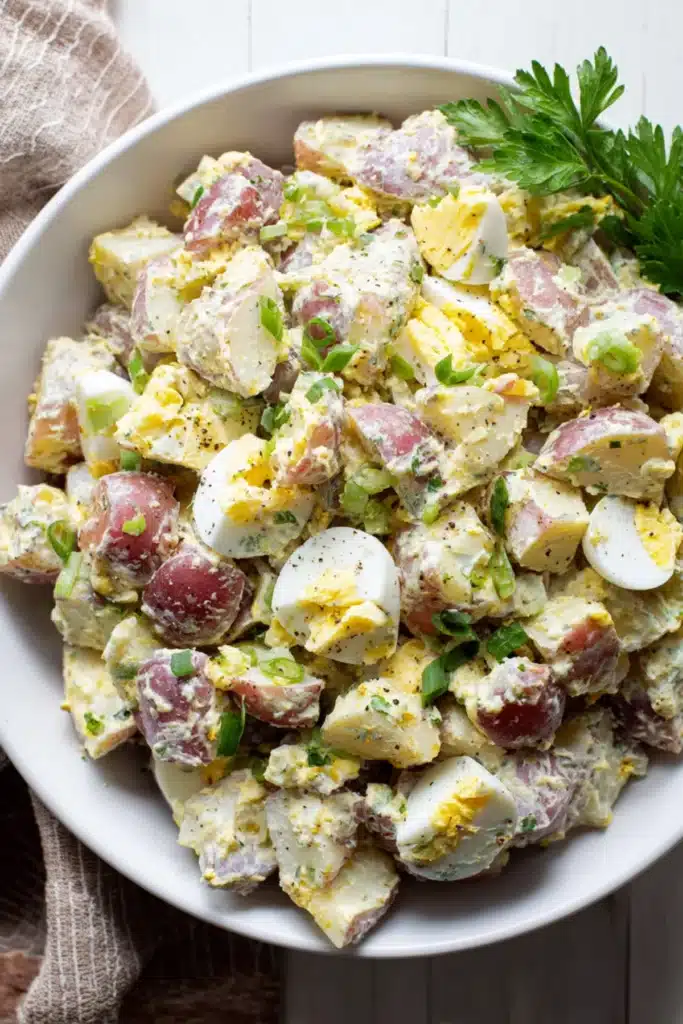 Red Hot and Blue potato salad with red potatoes, chopped eggs, mustard dressing, green onions, and black pepper