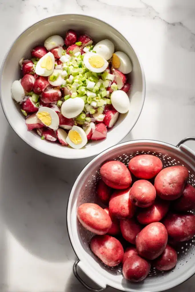 Ingredients for Red Hot and Blue potato salad with red potatoes, boiled eggs, and green onions in white bowls