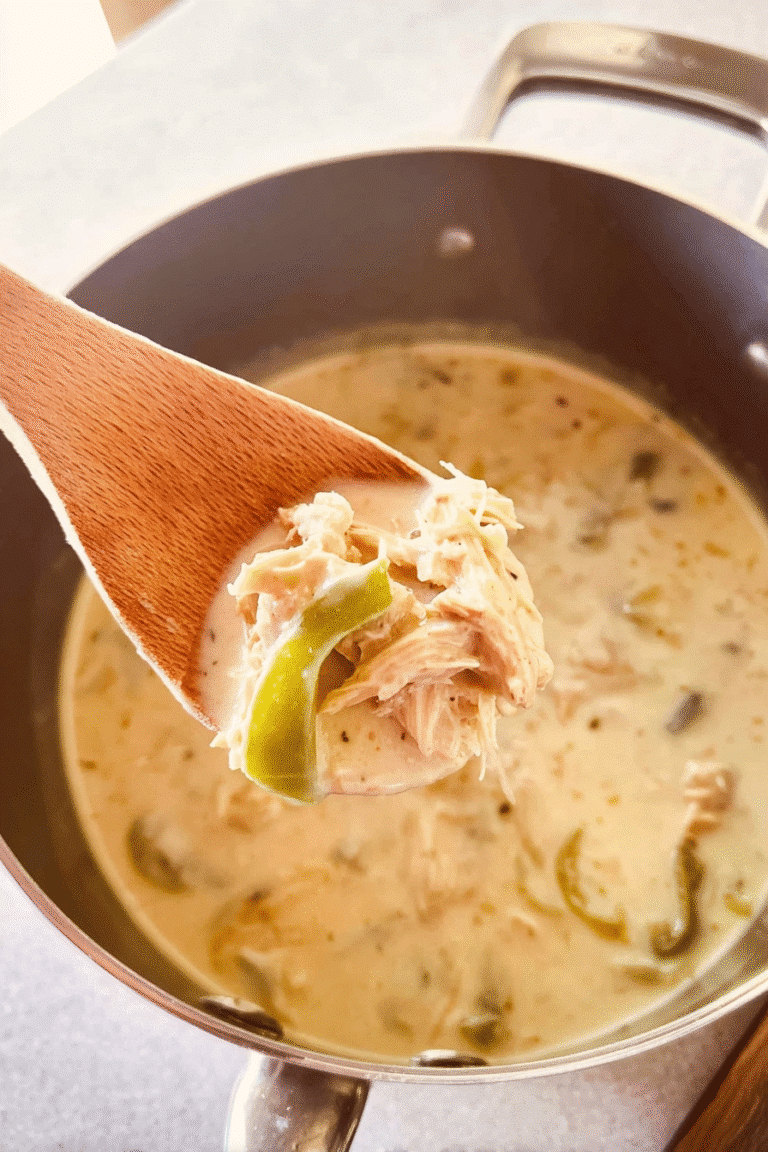 Creamy Cajun Chicken Soup simmering in a stainless steel pot, wooden ladle lifting a spoonful of creamy broth with shredded chicken