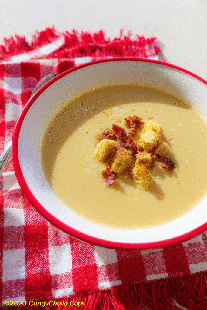Healing Garlic Soup for Colds served in a white bowl with red rim, creamy golden texture topped with crispy croutons and bits of roasted garlic