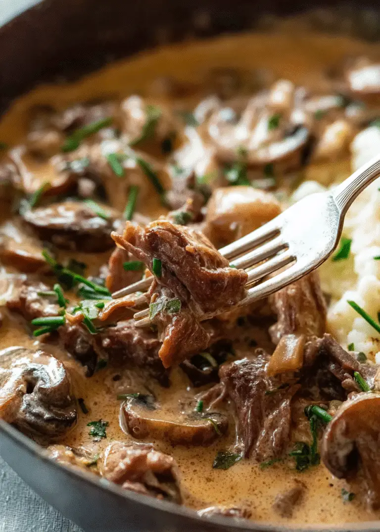 Forkful of tender slow-cooked beef with creamy mushroom sauce and fresh herbs for a rich and cozy Stroganoff meal.